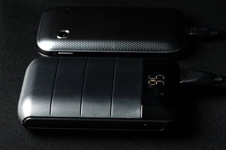 Charging the smartphone's battery with black power bank.