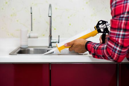 The man applying silicone sealant. The man fixing home.