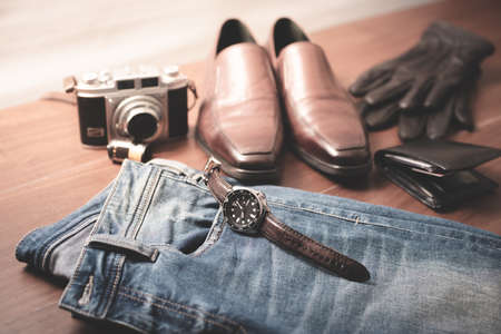 Men accessories on wooden desk. Closeup at luxury men watch with black dial and leather strap.
