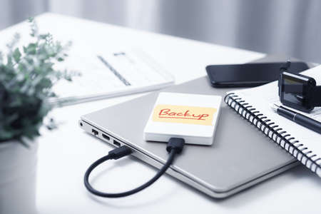 Closeup external hard drive with a tape labeled backup on white desktop. Working with external hard...