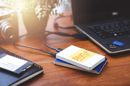 Closeup external hard drive with a tape labeled backup on wooden desktop. Working with external hard...