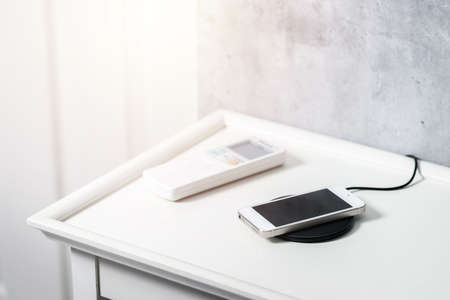 Charging the smartphone with wireless charger on the white desk.