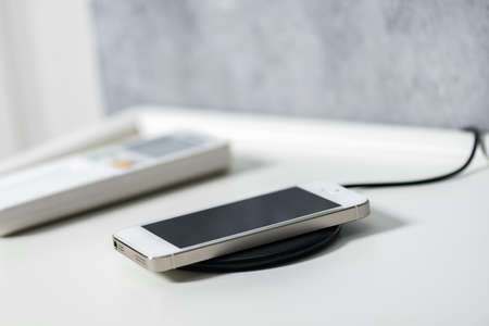 Charging the smartphone with wireless charger on the white desk.