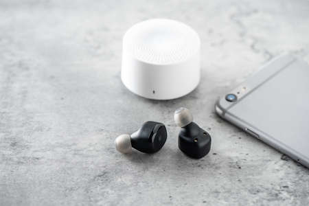 Pair of black true wireless earbuds with smartphone. Relaxation concept.