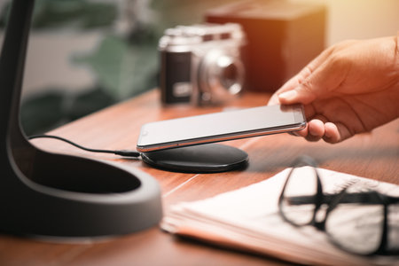 Charging the smartphone with wireless charger on wooden desk. Modern lifestyle concept.