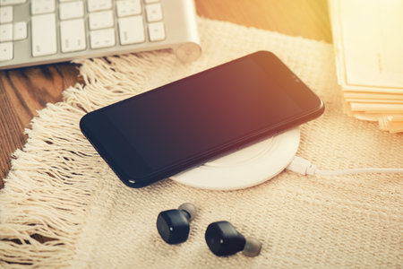 Charging the smartphone with wireless charger on wooden desk. Modern lifestyle concept.の写真素材