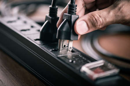 Closeup of a mans hand inserting a plug into electrical power strip.の写真素材