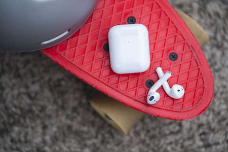 Pair of white wireless earbuds for smartphone on skateboard.