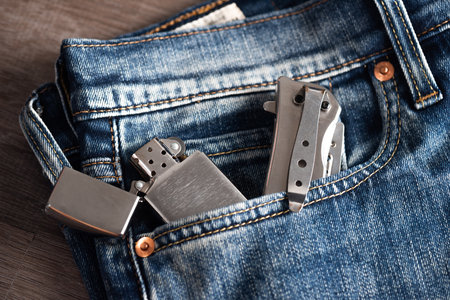 Close up stainless steel pocketknife and lighter on blue jeans. EDC (Every Day Carry) for men.の写真素材