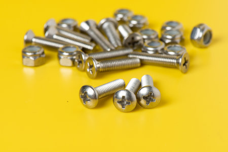Close up metal screws and nuts over yellow background.の写真素材