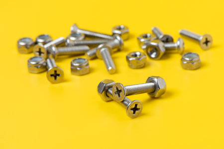 Close up metal screws and nuts over yellow background.