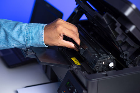 The man is repairing the laser printer, loaded black toner to the printer.