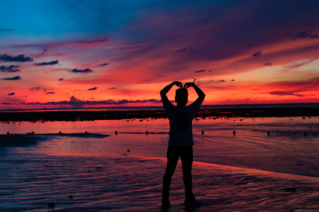 Man silhouette formed his arms as heart shape at the beach with sunset behindの写真素材