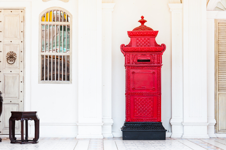 red and vintage postbox in front of an old building with stoolの写真素材