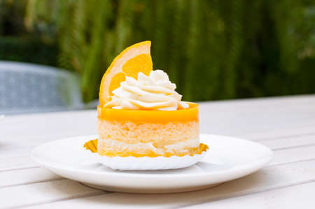 Orange cake on white plate and wooden table with cream and a piece of orange decorated toppingの写真素材