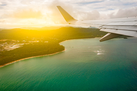 Airplane flying above beach blue sea island, taken from window with wing and, light filter, Phuket Thailandの写真素材