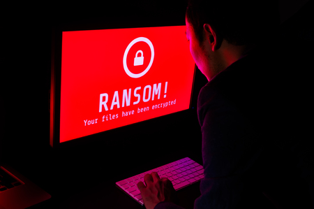 Computer screen with ransomware attack file encrypted alerts in red and a man in suit keying on keyboard in a dark room, ideal for online security and digital crimeの写真素材