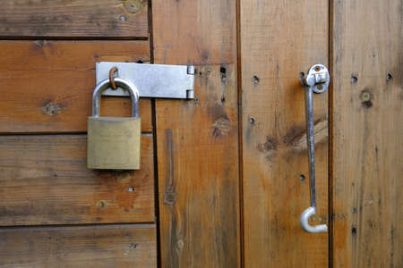 20 Oct 2019, Leeds, UK. Wodden built garden shed door, secured by a brass padlock and steel clasp. A hook bar hangs to the right of the lock.のeditorial素材