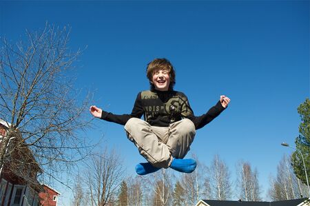 Jumping happy boy on blue sky backgroundの写真素材