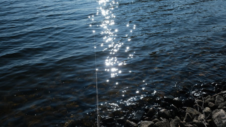 A fly fishing rod and an open fly fishing box lie on the rocks of a mountain river.