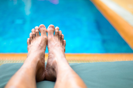 Feet of man laying beside swimming poolの写真素材