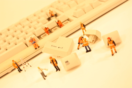A close up view of miniature plastic figures working on a computer keyboard.の写真素材