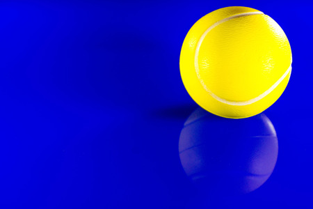 A closeup of a bright yellow tennis ball against a reflective blue background.の写真素材