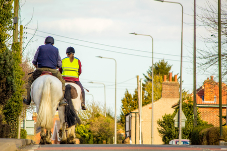 Two horse riders travel through a small village, on the main road.の写真素材