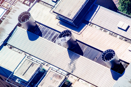 A view from above, looking down onto an industrial rooftop where chimneys expel steam.の写真素材