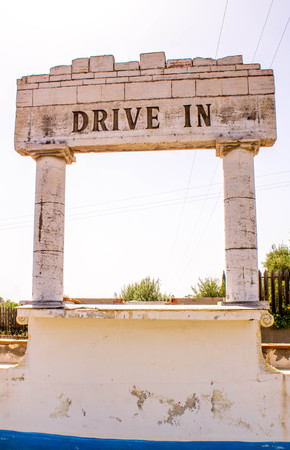 Sicily, Italy. An old drive through cinema in the outdoors of Sicily, now sits derelict with a concrete structure still showing the words 'Drive In' on it.の写真素材