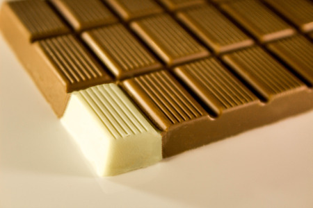 A bar of brown chocolate with just one square of white chocolate on the corner.の写真素材