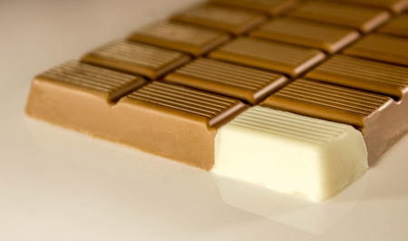 A bar of brown chocolate with just one square of white chocolate on the corner.の写真素材