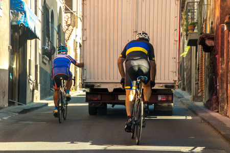 A cyclist chooses the easy / lazy option of holding onto the back of a truck to get up a hill.