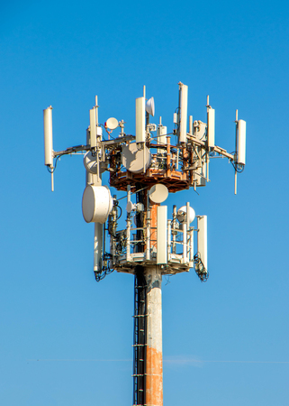 The top of a telecommunications tower against a plain blue, sky, background.