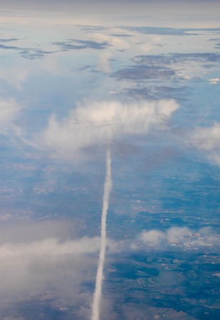 A view from altitude of an aircraft flying through the skies, its trails shown behind it.の写真素材