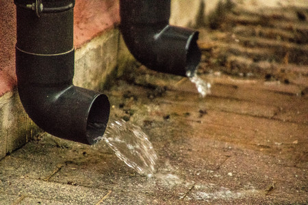 Two household gutters gushing with water from a heavy downpour of rain.