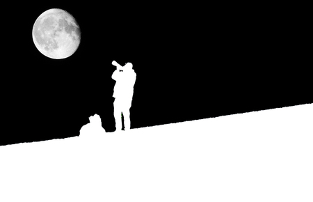 A black and white image of a silhouetted photographer on a hill taking a photo of the Moon.の写真素材