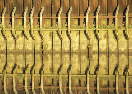 The reflection of a dock / harbour wall in calm still river water, on a sunny day.の写真素材