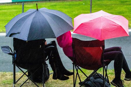 22nd September 2019 - Cadwell Racetrack, Lincolnshire, England. Two spectators on camp chairs, with umbrellas, brave the downpour of rain as all other spectators have gone home.の写真素材