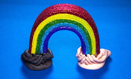 Two sets of cupped hands, both different races, hold each end of a rainbow.の写真素材