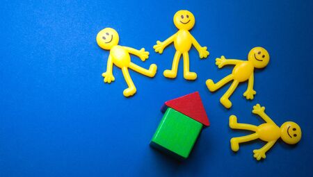 Yellow toy figure people stand by a wooden block house. The house possibly rented or a new...