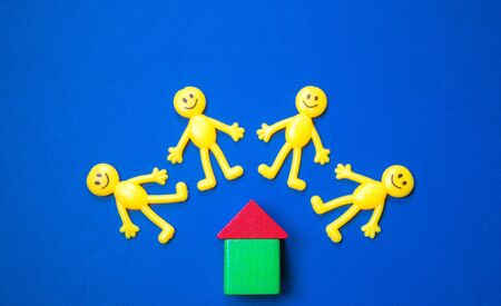 Yellow toy figure people stand by a wooden block house. The house possibly rented or a new...