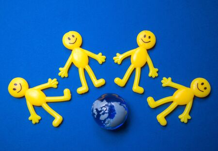 Yellow figure people surround the top of a miniature version of planet Earth.