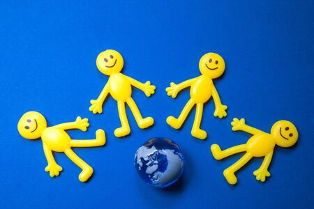 Yellow figure people surround the top of a miniature version of planet Earth.の写真素材