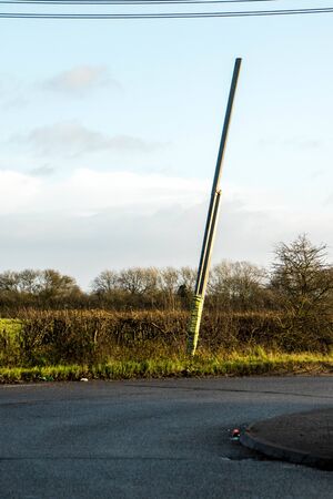 A large telegraph pole lays at a dangerous angle due to it being hit by a vehicle. The bottom half taped up with Police tape who are aware of it.の写真素材