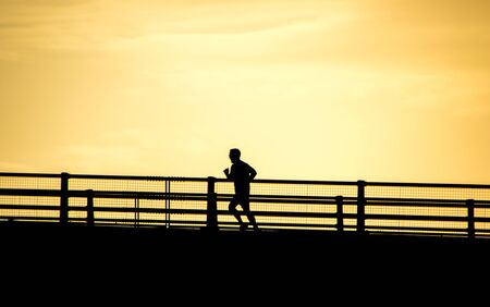 An adult male running across a motorway bridge while he tries to improve his health / fitness.の写真素材