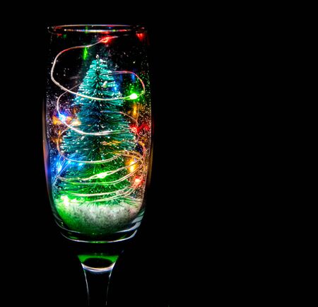 A champagne glass with a Christmas tree, lights and snow bringing that festive celebration.の写真素材
