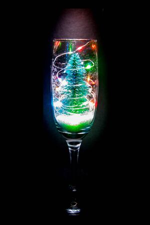 A champagne glass with a Christmas tree, lights and snow bringing that festive celebration.の写真素材