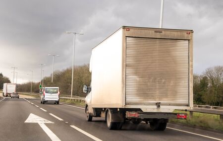 A 'white' van traveling along a main road in the United Kingdom, the roads wet and dirty.
