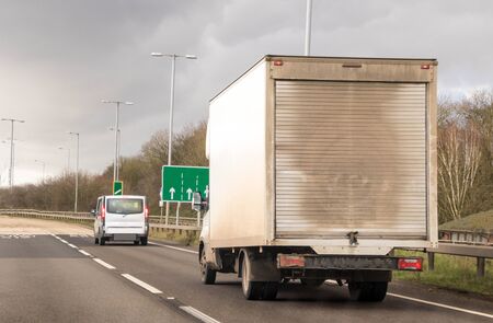 A 'white' van traveling along a main road in the United Kingdom, the roads wet and dirty.の写真素材